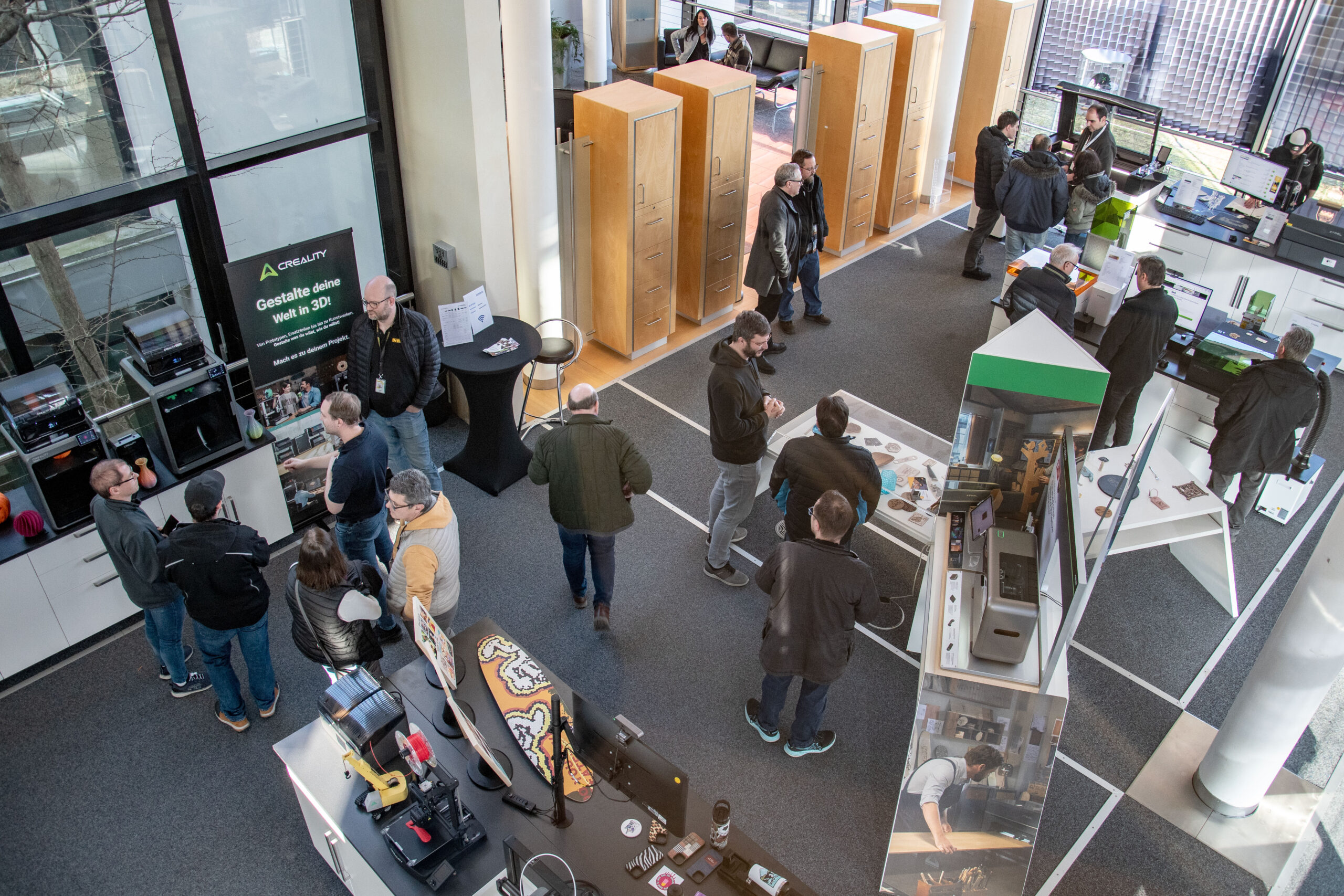 In diesem Bild sind verschiedene Menschen zu sehen, die in einem Raum mit verschiedenen Lasern und 3D-Druckern stehen