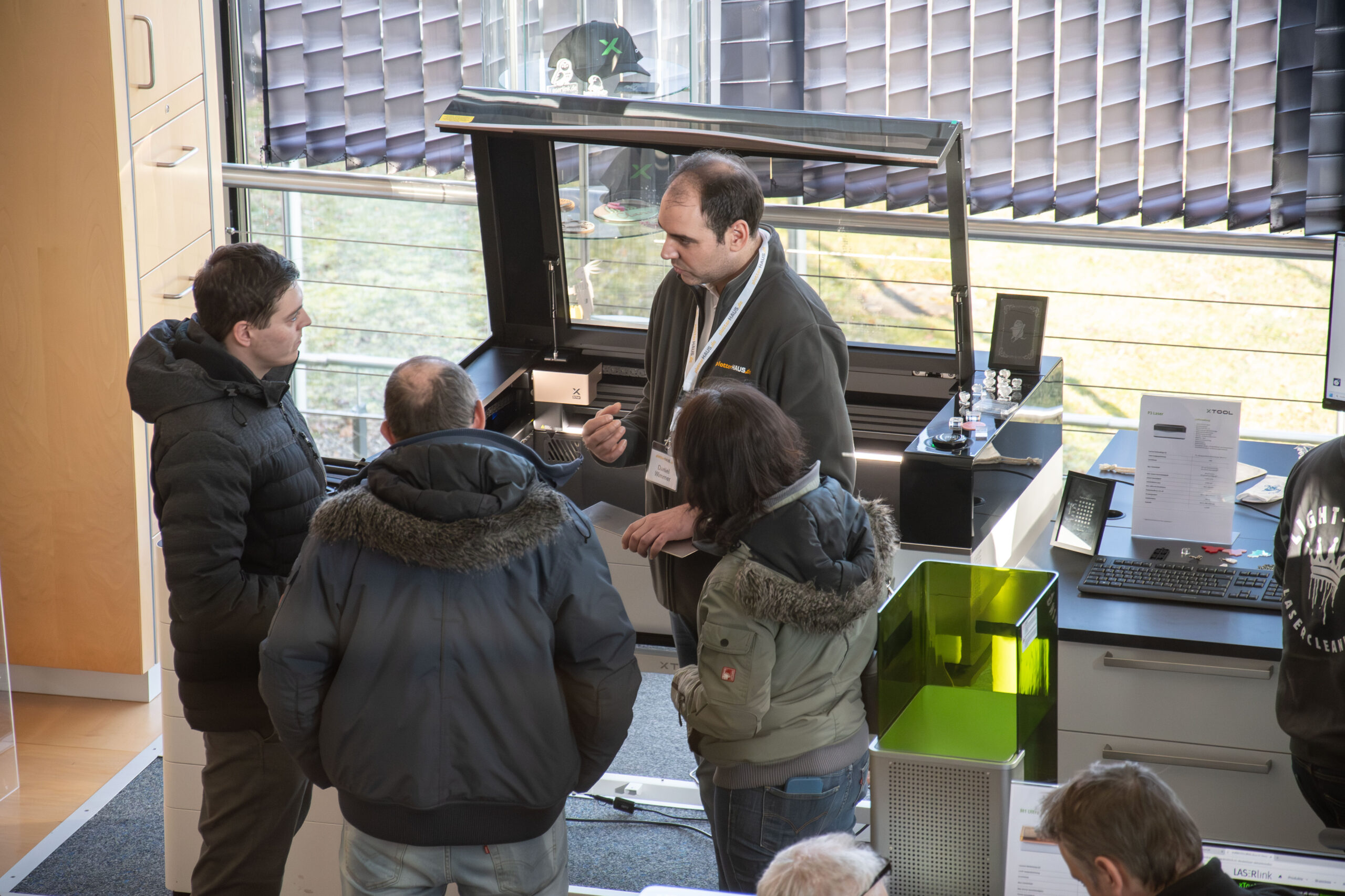Ein PlotterHAUSmitarbeiter berät drei Kunden vor einem xTool P2S Lasergerät
