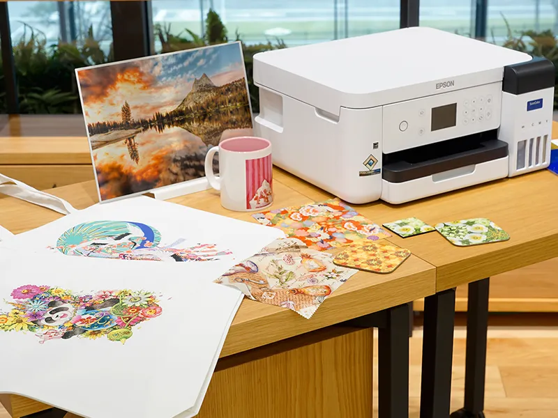 Der SureColor Sublimationsdrucker von Epson auf einem Tisch der mit vielen Sublimierten Mustern dekoriert ist.